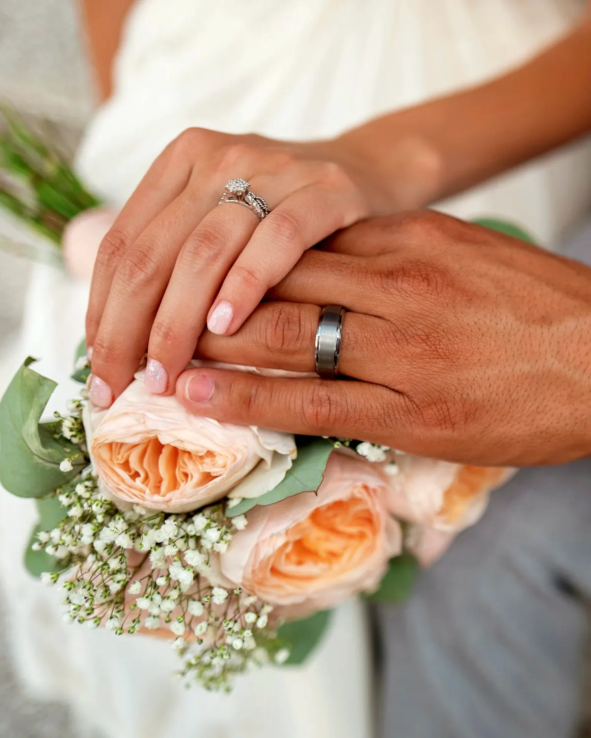 Mains des mariés réunies sur le bouquet, alliances bien visibles