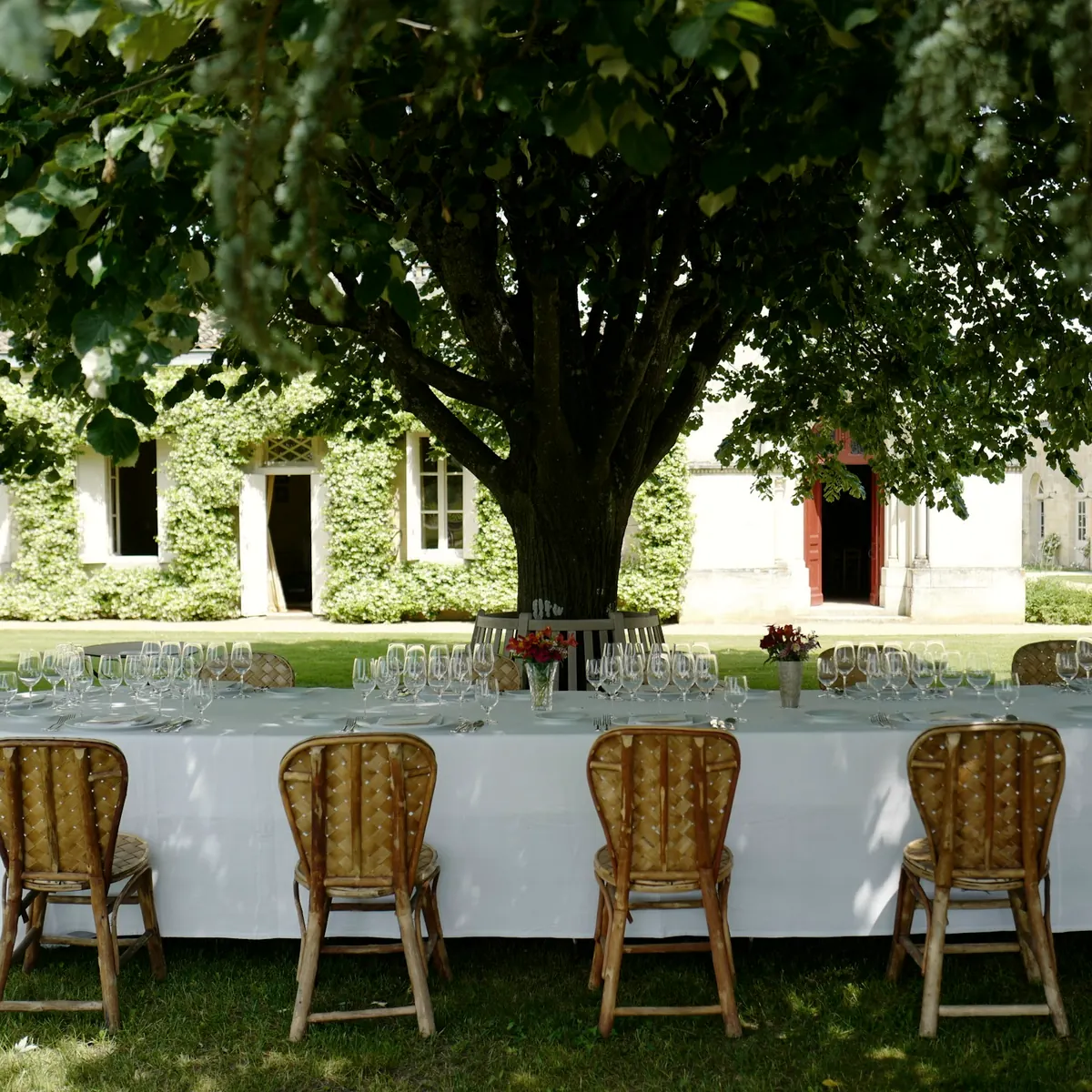 Table de réception dressée à l’ombre d’un arbre devant une demeure en pierre